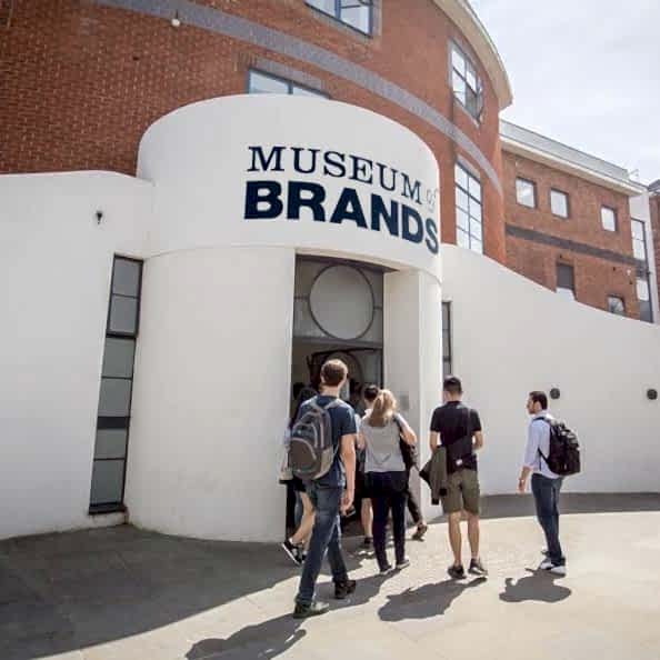 A group of people walk into The Museum of Brands, a white building with Museum of Brands written on the front.