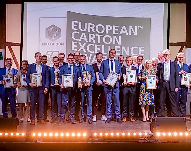 A large group of people in formal clothes holding certificates, in front of a screen with text that reads 'European Carton Excellence Awards'